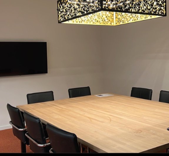 Een opgeruimde vergaderzaal met houten tafel en zwarte stoelen